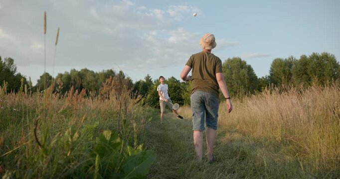 Two boys play badminton on nature. Teenagers spending time together. 4K 10-bit