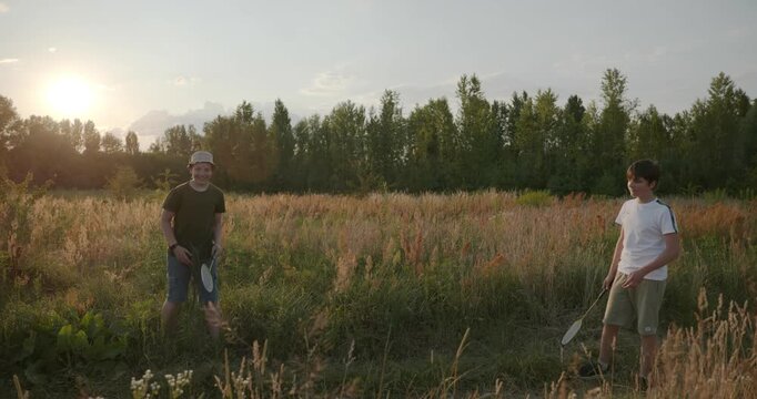 Two boys play badminton on nature. Teenagers spending time together. 4K 10-bit