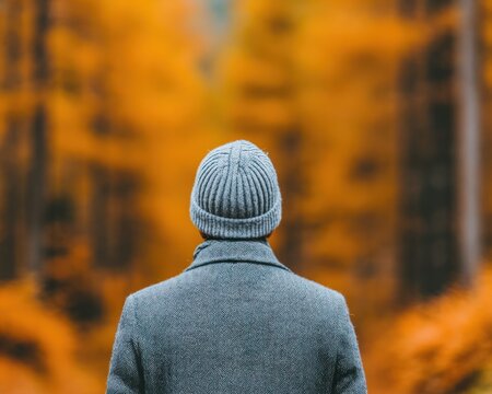 Person wearing grey wool coat and beanie standing in forest with vibrant orange autumn foliage during crisp fall day for seasonal lifestyle imagery