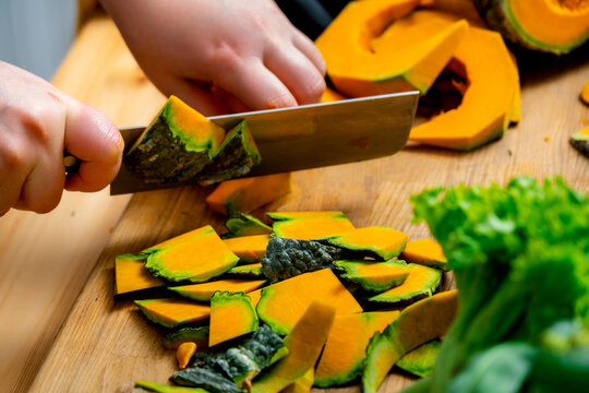 Woman hands chop green skin pumpkin into small pieces. Raw vegan food ingredient preparation concept.