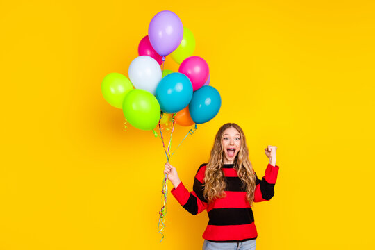 A cheerful girl in a striped sweater holding colorful balloons on a bright yellow background showcases a festive mood