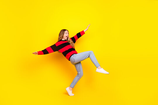 Cheerful young woman in a striped sweater posing playfully against a vibrant yellow background, expressing energy and fun