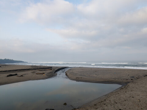 Scenic Black Sand Beach with Small River Estuary Flowing into the Ocean Under Cloudy Sky