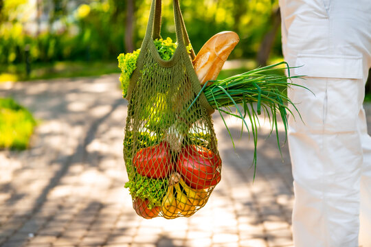 Woman carries green string mesh bag with fresh food in park. Eco friendly zero waste concept.