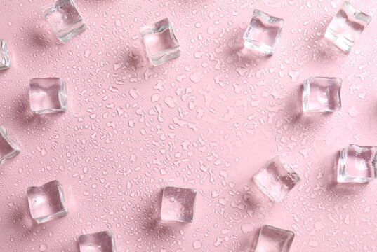 Ice cubes and water drops on pink background, top view