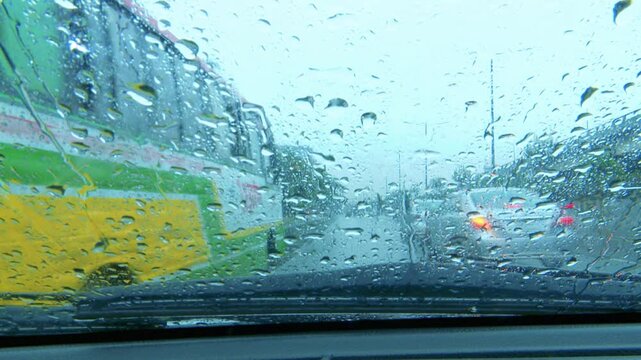 Colorful bus and traffic viewed through rain covered windshield on a wet road