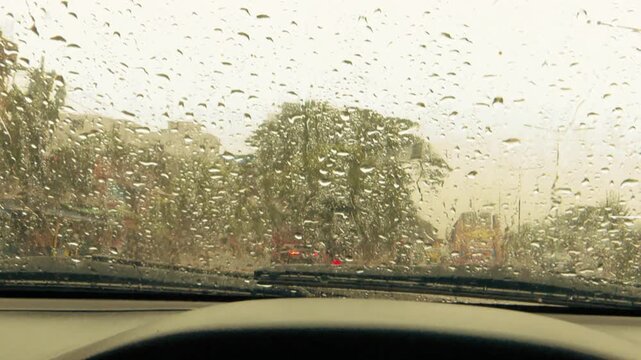Heavy raindrops covering windshield with blurred trees and road in monsoon weather