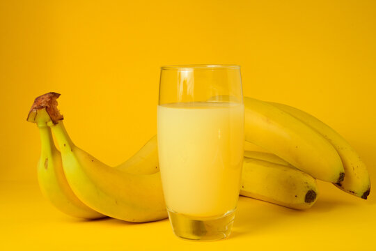 Vaso de zumo de platano natural acompa&ntilde;ado de platanos frescos sobre un fondo amarillo. Concepto de alimentaci&oacute;n saludable, bebida refrescante, fruta de verano y fotograf&iacute;a de producto en estudio 