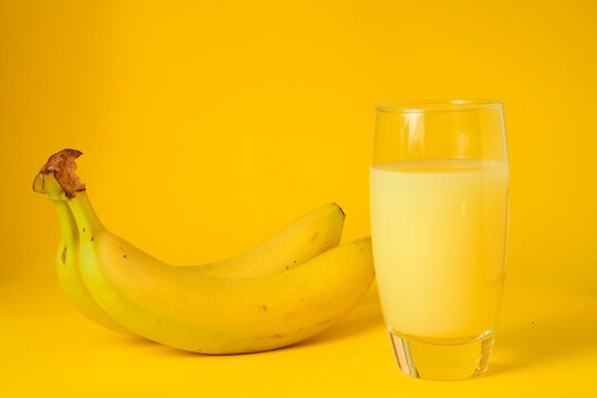 Vaso de zumo de platano natural acompa&ntilde;ado de platanos frescos sobre un fondo amarillo. Concepto de alimentaci&oacute;n saludable, bebida refrescante, fruta de verano y fotograf&iacute;a de producto en estudio 