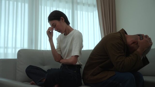 Heartbroken couple sitting apart after an unresolved family conflict at home. Relationship challenges, emotional stress. Communication breakdown, financial pressure. Mental wellbeing and marriage.
