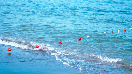 Red and white safety buoys on a rope line floating in the sea water near the beach shore. © Наталья Добровольска