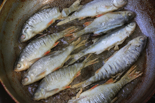 Small whole fish being fried in a rustic pan with oil