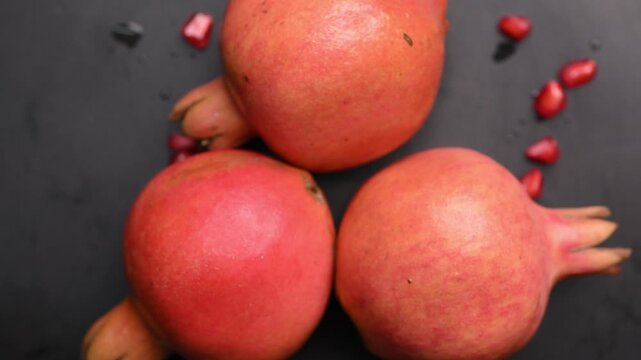 Rotating Fresh Anar Pomegranates in Top View with Scattered Seeds on Dark Surface