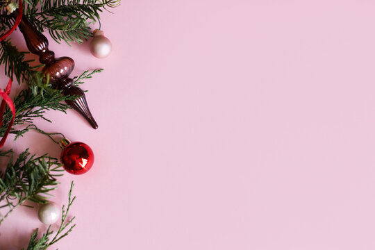 Christmas background. Elegant vintage glass finial ornament, red bauble and ribbon on fir branch on pastel pink background with copy space. Xmas flat lay