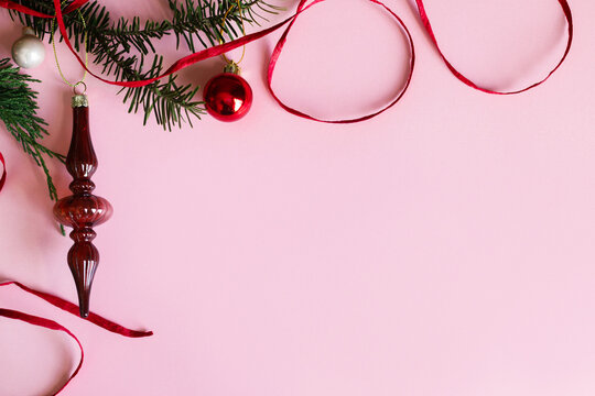 Christmas background. Elegant vintage glass finial ornament, red bauble and ribbon on fir branch on pastel pink background with copy space. Xmas flat lay
