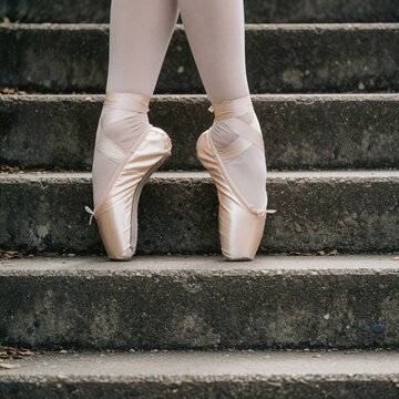 Ballerina feet in pointe shoes stand on stone stpic. Elegant dancer poised on outdoor staircase. Graceful pose outside on cement stairs during day.