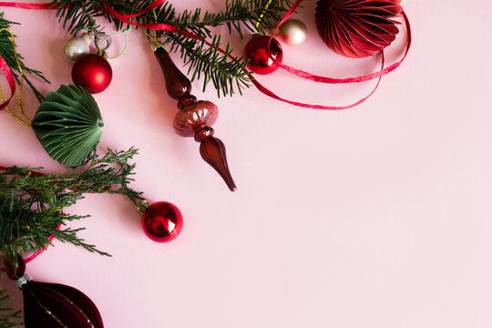 Elegant Christmas flat lay border with paper ornaments, red baubles, glass finial, and fir branches on pastel pink background. Xmas background with copy space. Merry Christmas