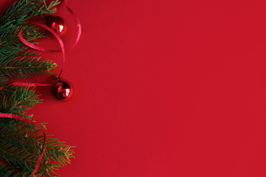 Shiny red christmas baubles and ribbon on fir branches forming border on rich red paper background with copy space
