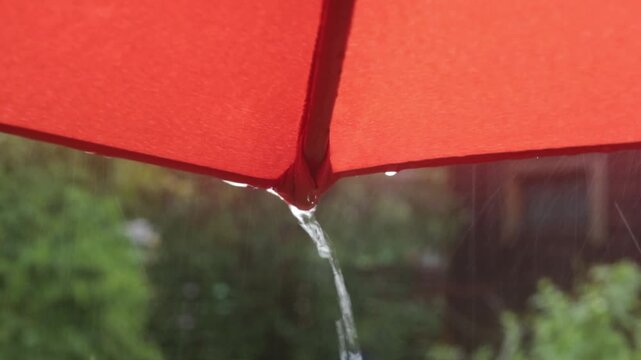 Water streams from the tip of a red umbrella during heavy rain, close-up of rain protection, wet weather, outdoor lifestyle, rainy day concept.