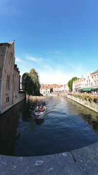 Vertical timelapse from a bridge in Bruges of several tour boats passing on the canal and people walking along the Dijver, Belgium