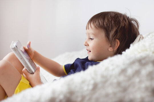 Close-up side view of a smiling boy sitting on a comfy sofa using a digital tablet