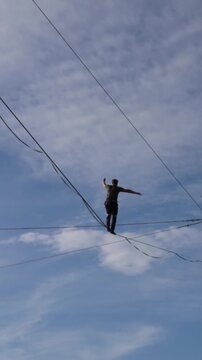 A highwire performer balances alone against a blue sky, creating a dramatic concept of courage, freedom and adventure.
