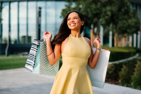 Smiling woman enjoying retail therapy, carrying colorful shopping bags after a successful day of shopping in an urban environment