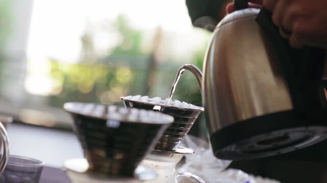 barista pouring hot water from kettle into coffee dripper for pour over brewing method