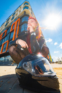 Stylish red haired woman with motorcycle helmet posing near modern building with copy space