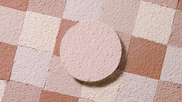 Overhead slow-motion capture of fine beige powder sifted in a round shape over a beige to brown square mosaic background, propelled outward by airflow | Commercial idea for foundation