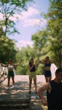 A group of active friends enjoys a fitness walk across a wooden bridge in a sunny park. They celebrate their strength and healthy lifestyle together outdoors.