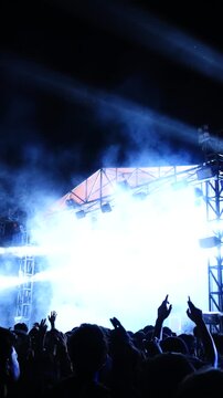 Vertical video of a concert crowd surrounded by colorful stage smoke and lights