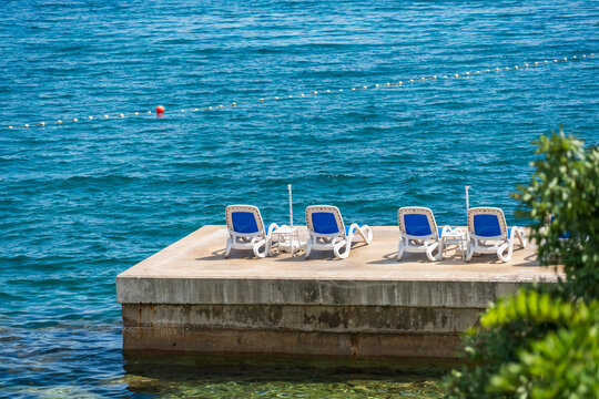 Empty sun loungers on a seaside platform above crystal-clear Adriatic waters, creating a peaceful summer holiday atmosphere