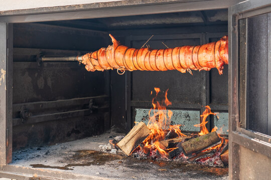 Whole pig slowly roasting over an open wood fire inside a large barbecue oven, showcasing traditional Balkan and Croatian outdoor cooking
