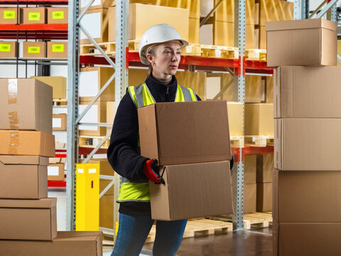 Warehouse logistics. Worker handles cardboard boxes in a storage facility, preparing goods for inventory, order fulfillment, packaging and distribution.