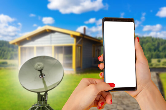 Satellite internet. User accesses broadband communication by smartphone through a satellite antenna at a rural home, providing remote connectivity and online services.