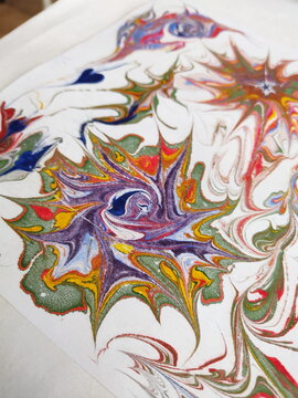 Colorful ebru art swirls with vibrant patterns on a white water surface.