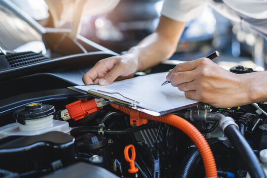 Auto check up and car service shop concept. Mechanic writing job checklist to clipboard to estimate repair quotation to client at workshop garage