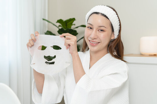 Beautiful Asian woman holding sheet mask off her face for skincare routine.