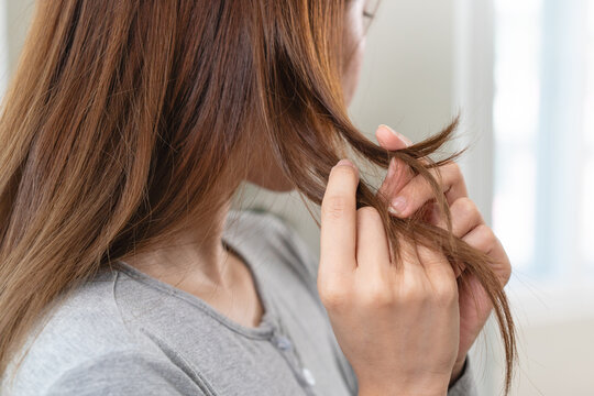 Close-up of a young woman holding and examining her damaged hair split ends.