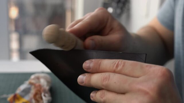 Craftsman burnishing a leather edge with a wooden slicker in a workshop for handcrafted products