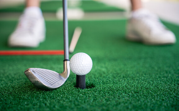 Golf Practice Close-Up of an Iron Club beside a Ball on a Tee over a Green Hitting Mat at an Outdoor Driving Range