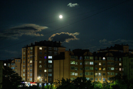 Full moon shining in dark sky over residential buildings with lit windows at night.