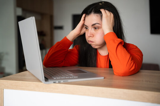 Frustrated young woman staring at laptop screen in home setting. Digital burnout online learning stress and technical issues