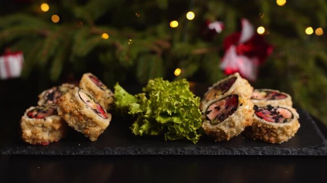Delicious fried sushi rolls with salmon served on a stone slate plate during christmas with festive bokeh lights and a decorated tree in the background for a holiday meal