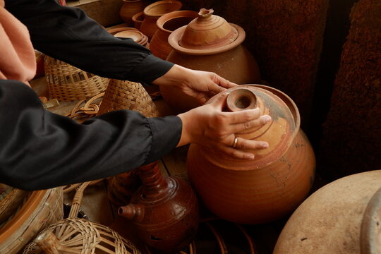 Customer examining brown terracotta pot at traditional artisan pottery store
