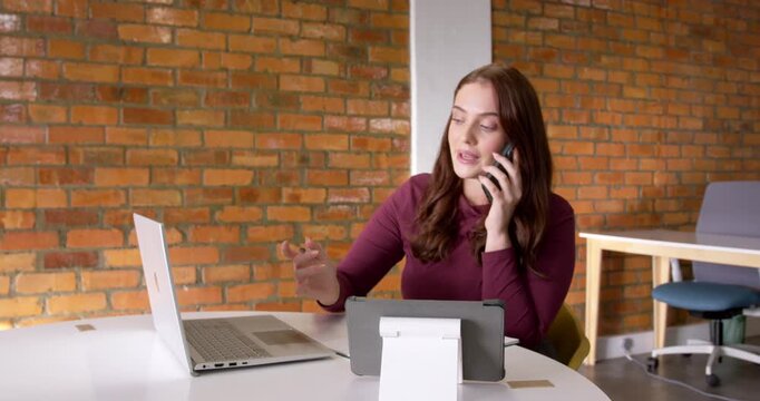 Adult female taking work call, pointing pen at laptop or tablet, ending call, tapping phone at offic