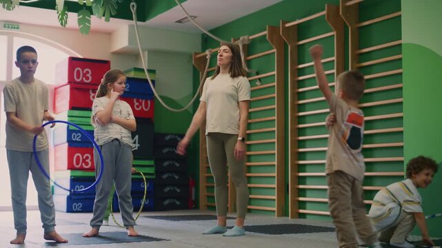 Young children enthusiastically exercise with colorful hula hoops alongside their instructor in a modern gym. Kids engage in active play and physical activity for health and development.