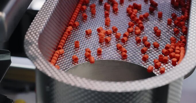 Vibrating mesh sorter moves red capsules toward central opening in pharmaceutical line. Controlled motion separates medicine units as feed-processing stage