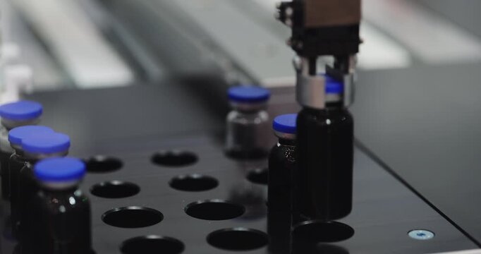 Robotic gripper places capped vials into circular tray on automated line. Precision mechanism positions each container for controlled pharmaceutical sorting